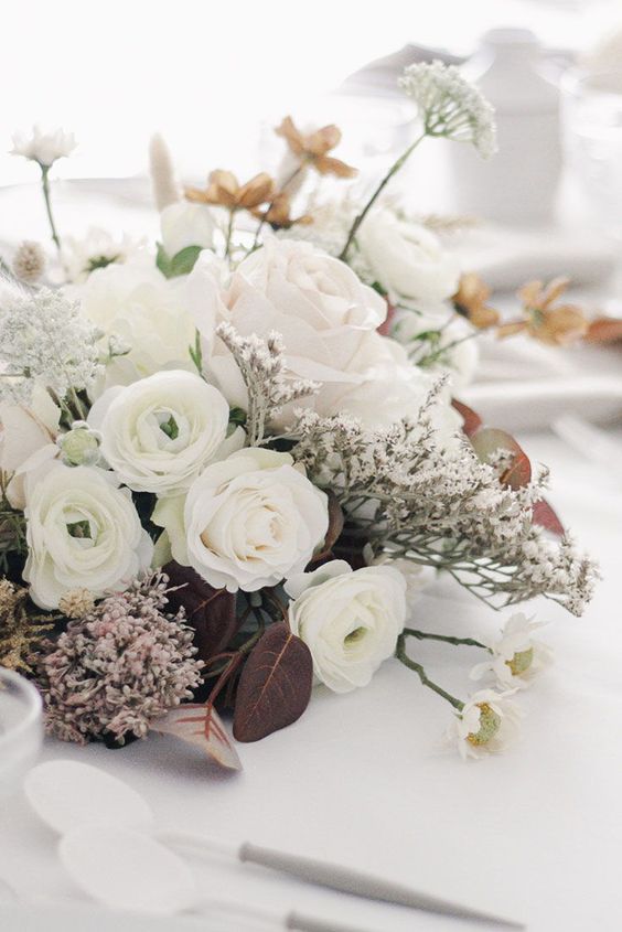 a refined and chic contrasting wedding centerpiece with white roses, ranunculus, dark foliage and waxflower is a lovely idea to rock