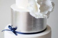 a refined and chic wedding cake with white lace tiers, a silver leaf tier and a large sugar bloom plus a navy ribbon with a bow