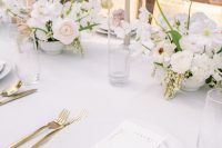 a refined modern wedding table setting with white linens and porcelain, a blush, white and yellow floral centerpiece and gold cutlery