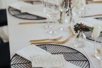 a refined modern wedding tablescape with geometric black placemats, gold cutlery, white blooms and leaves and tall and thin candles