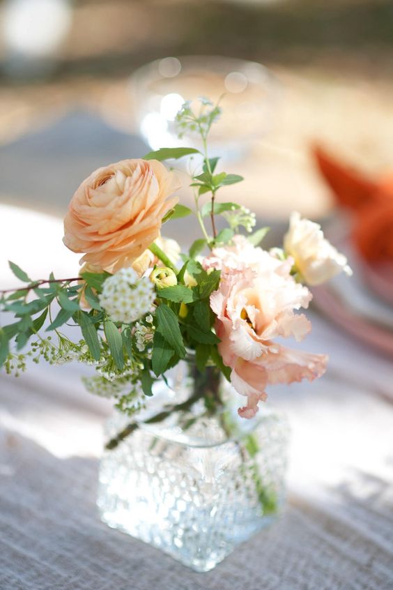 a refined wedding centerpiece of a vintage crystal vase, orange ranunculus, pink and white blooms and greenery for a summer wedding