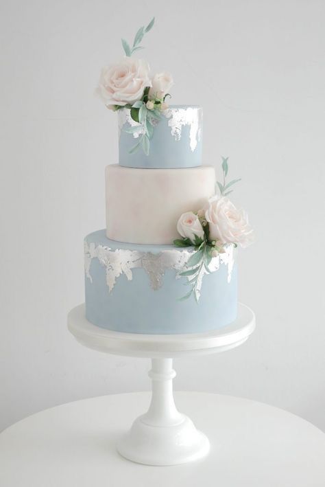 a serenity blue and white wedding cake with silver leaf, white and blush blooms and greenery is a delicate and beautiful idea