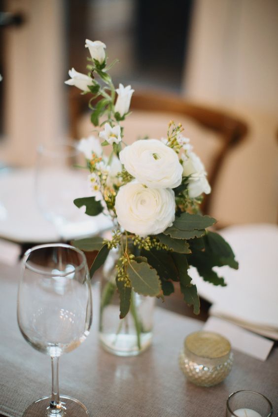 a simple and delicate wedding centerpiece of a clear vase, white blooms and ranunculus, greenery is a stylish idea to recreate