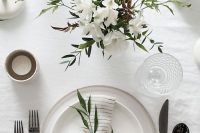 a stylish and simple neutral wedding tablescape with a neutral floral centerpiece, neutral porcelain, black cutlery, candles is chic