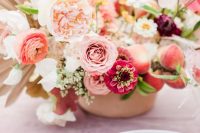 a super lush and whimsical wedding centerpiece of pink and orange ranunculus, hot pink blooms and peony roses and fronds and peaches