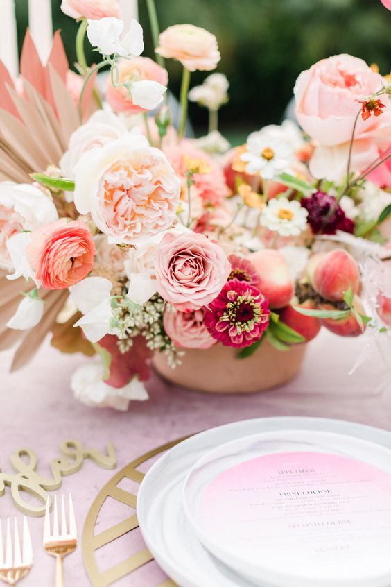 a super lush and whimsical wedding centerpiece of pink and orange ranunculus, hot pink blooms and peony roses and fronds and peaches