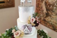 a white and silver glitter wedding cake with silver leaf, with Harry Potter signs, pink blooms, Snitch, silver deer and a calligraphy topper