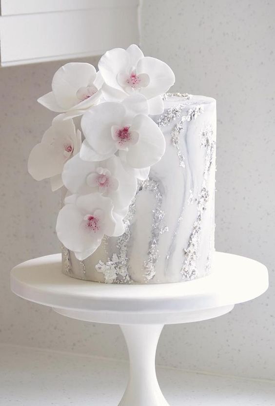 a white marble wedding cake with silver leaf and white orchids is a stylish and chic idea for a modern wedding with a refined feel