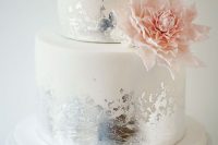 a white wedding cake with silver leaf, a pink bloom is a stylish and shiny idea of a wedding cake for spring or summer