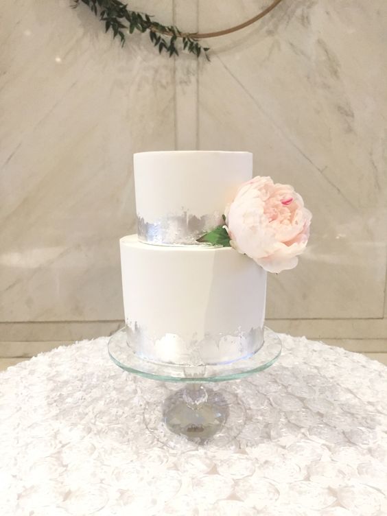 a white wedding cake with silver leaf, with a large blush bloom and greenery is a beautiful and refined idea for a modern wedding