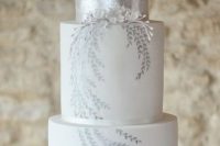 a white wedding cake with silver leaf with silver leaves painted, with white sugar blooms is a delicate and elegant wedding idea