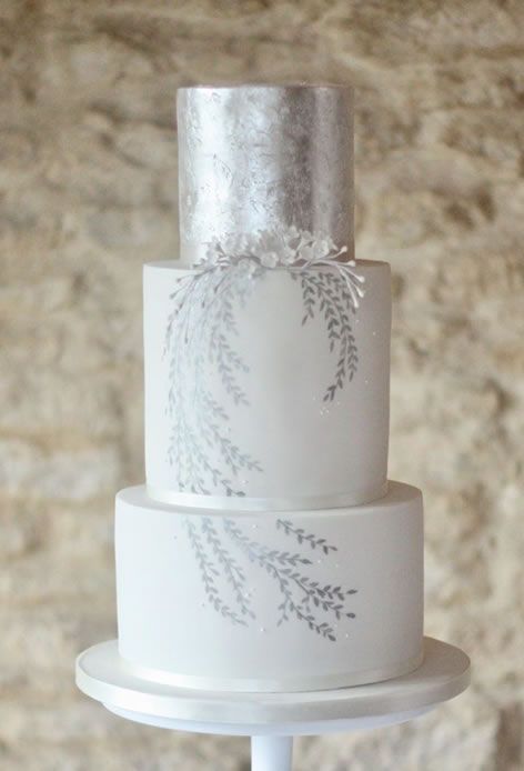 a white wedding cake with silver leaf with silver leaves painted, with white sugar blooms is a delicate and elegant wedding idea