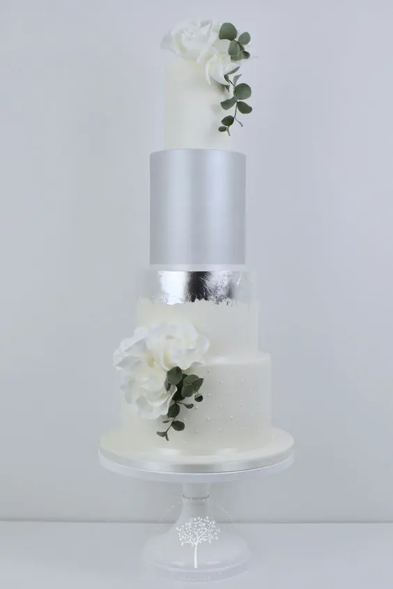 a white wedding cake with white tiers, a matte silver and a silver leaf tier, white blooms and greenery is a very chic idea