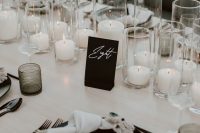 an elegant modern wedding tablescape with pillar candles, black plates and cutlery, black glasses and a card is chic