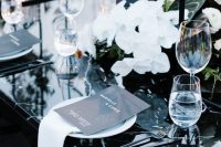 an exquisite modern wedding tablescape with a black marble table, white orchids and leaves, black menus and candles is amazing