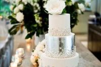 a glam wedding cake with white and silver tiers, beads and edible lace plus a white bloom on top is very refined