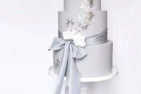 a grey plain wedding cake with silver leaf, white blooms and a long ribbon with a bow is a stylish modern wedding dessert