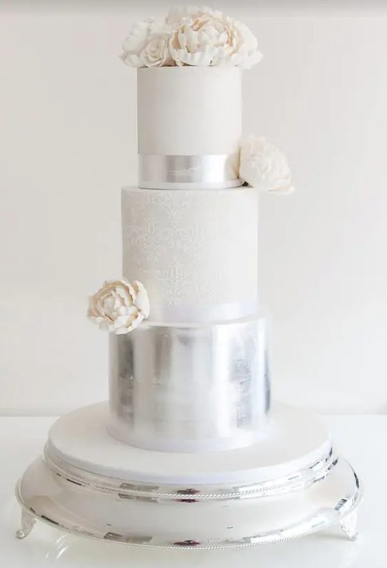 a large vintage-inspired wedding cake with a silver, white patterned and white sleek tier, white sugar blooms is wow