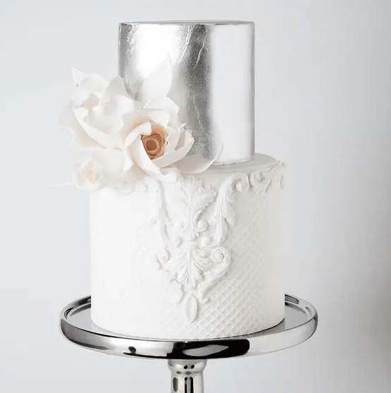 a refined vintage wedding cake with a silver leaf and white patterned tier and some white sugar blooms