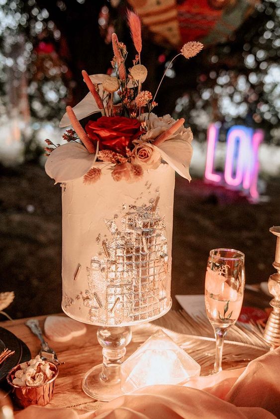 a unique boho wedding cake with disco ball part, some dried blooms and leaves on top is wow