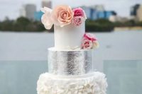 a white cake with a ruffled and a silver tier, bold flowers on top is a catchy glam dessert for a glam wedding