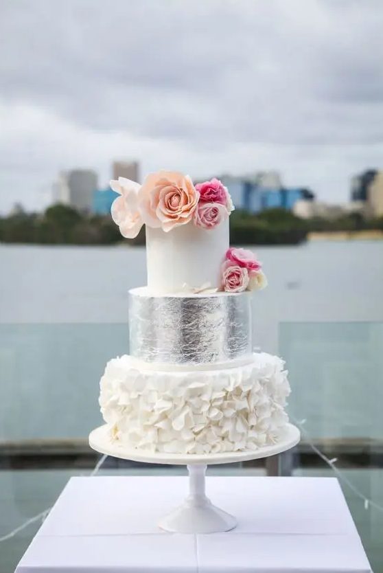 a white cake with a ruffled and a silver tier, bold flowers on top is a catchy glam dessert for a glam wedding