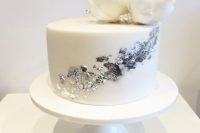a white wedding cake decorated with silver leaf and with white sugar blooms on top is a cool and catchy wedding dessert