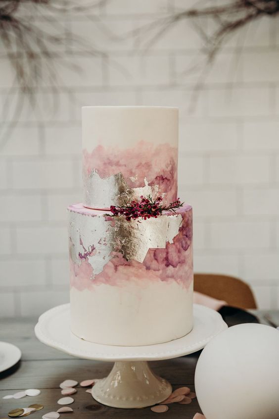 a white wedding cake with pink watercolor and silver leaf is a unique idea for a pink wedding