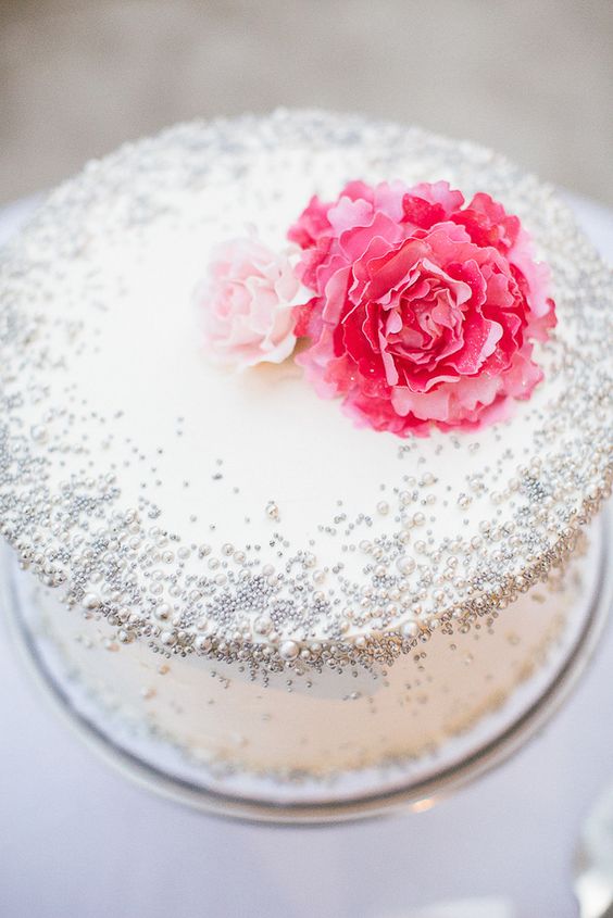 a white wedding cake with silver beads and pink blooms on top is a cool idea for a glam wedding