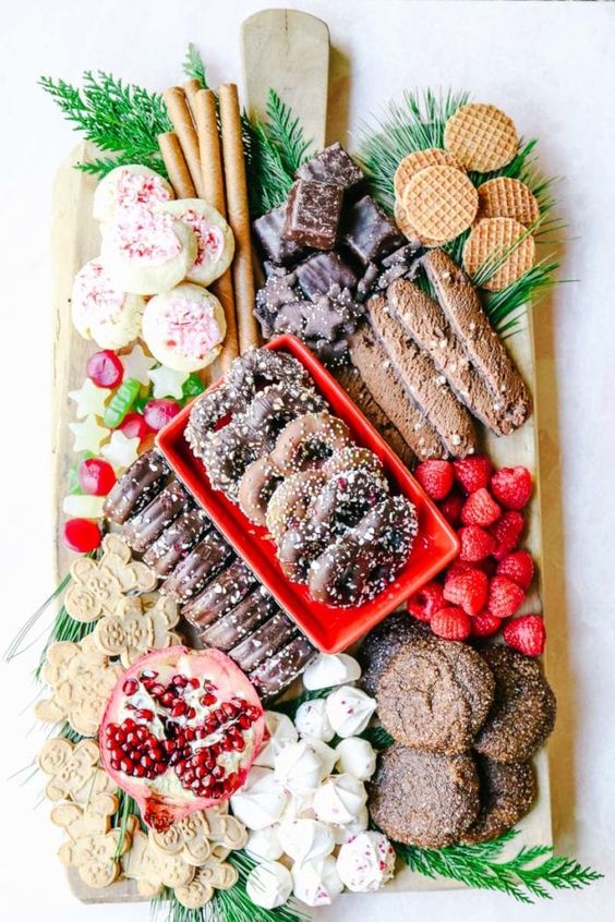 a Christmas dessert board filled with yummy cookies and treats, with meringues, pomegranates, herbs, fresh berries and waffles