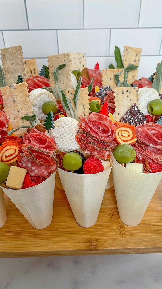 a board with charcuterie cones with candies, fresh fruit and berries, salami and hat, cookies and cheese are amazing for a wedding