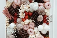 a chic and refined wedding dessert board with various glazed donuts and cookies, meringues, Oreos, popcorn and strawberries and figs