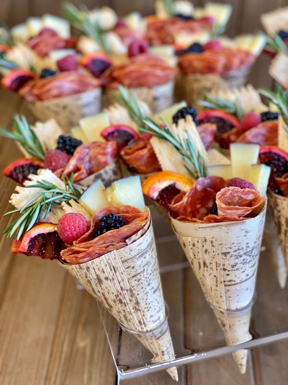 a clear acrylic stand with cones with charcuterie - cheese, berries, salami, fruit and herbs is a lovely idea to rock at your wedding