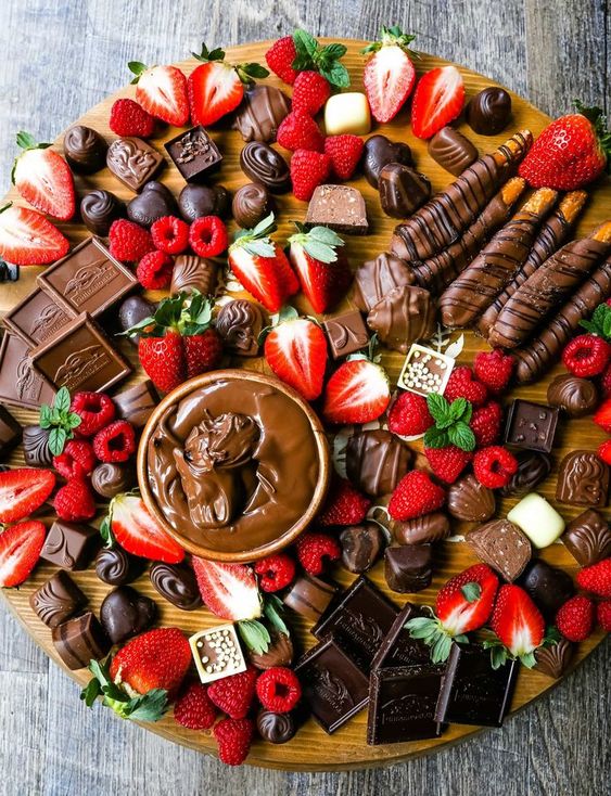 a decadent chocolate board with an assortment of chocolate truffles, milk chocolate, dark chocolate hearts, chocolate covered pretzels, Nutella, berries