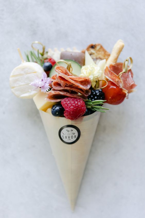 a delicious mini charcuterie cone with salami, various types of cheese, fresh fruit and berries, crackers and herbs are wow