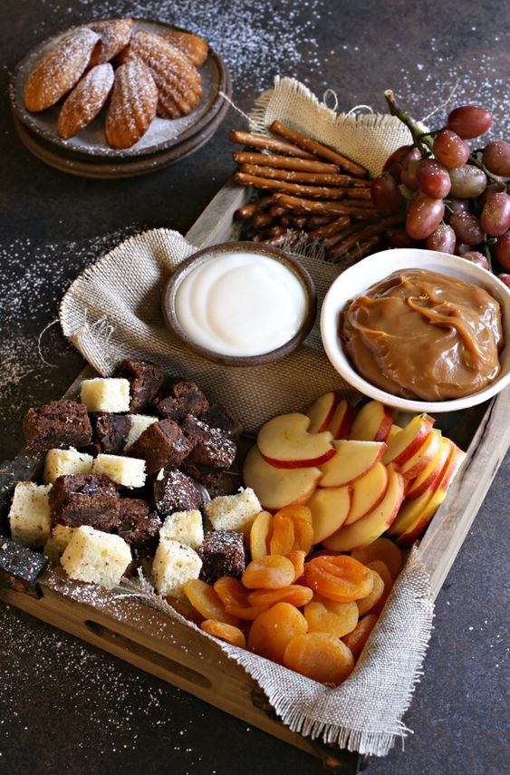 a fall wedding dessert board with apples, apricots, salty sticks, various dips and caramel, cake pieces and grapes is amazing