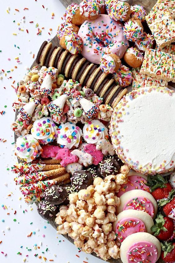 a fantastic dessert grazign table with glazed funfetti cookies, chocolate, popcorn, waffles and a mini cake in the center