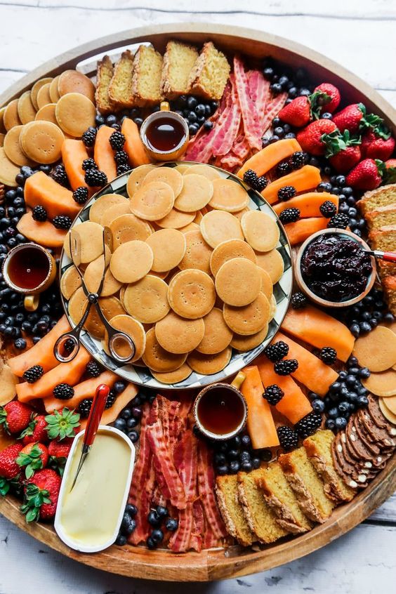 a gorgeous sweets board with pancakes, cookies, cakes, crackers, fresh fruit and berries, various kinds of dip and butter