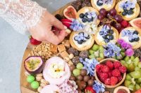 a gorgeous sweets platted with delicious pavlovas, blooms, floral cupcakes, fruits, nuts, cookies topped with fruit and other delicious desserts