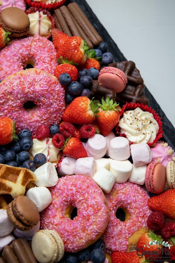 a slate-style platter with fresh berries, marshmallows, glazed donuts, cupcakes, macarons and meringues is a perfect idea for a party or a wedding