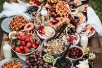 a sweet breakfast grazing table with fresh fruit and berries, waffles, various kinds of dip and compote, yogurt and croissants