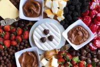 a sweet grazing platter with fresh berries, candies, chocolate, cakies, chocolate dip and a piece of cheese in the center