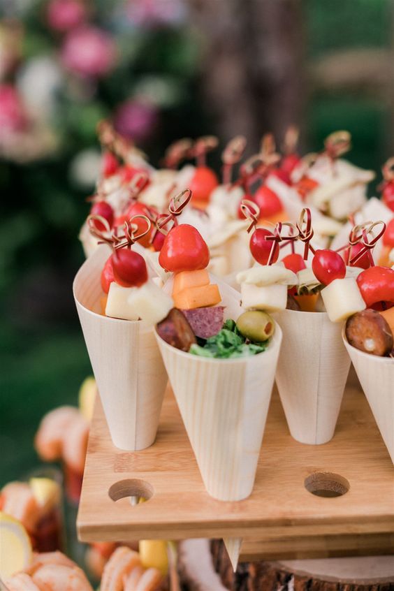 cool cardboard charcuterie cones with fresh tomatoes, olives, various types of cheese and salami, some greenery