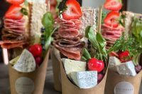 gorgeous charcuterie cups of cardboard, with various types of cheese, salami, fresh strawberries and cheeries, some herbs and greenery