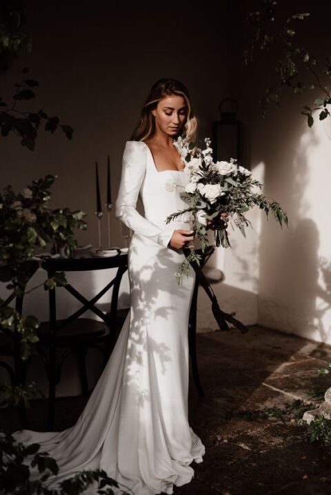 a modern plain mermaid wedding dress with a square neck, long sleeves with accented shoulders, a sash and a train is gorgeous for a modern wedding