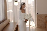 30 a stylish minimalist bridal look with a square neckline mermaid wedding dress, long sleeves and a train, a pearl headpiece and a veil