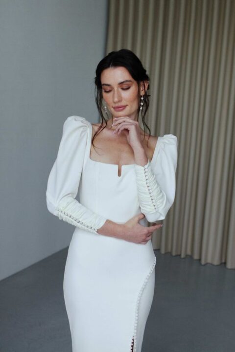 a beautiful and eye-catchy plain wedding dress with a square neckline, puff sleeves accented with buttons and a skirt with a slit that is also accented with buttons