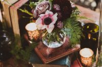 a beautiful dark enchanted forest wedding centerpiece of a stack of books, candles, a dark floral centerpiece and greenery