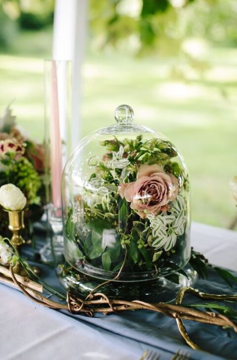 a blue table runner and a grey tablecloth, vine branches, a cloche with a pink bloom and some greenery, pink candles for an enchanted forest wedding