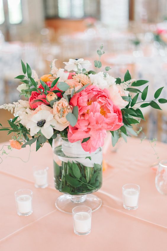 a bold wedding centerpiece of white, bold pink and orange blooms and greenery and candles around is a gorgeous idea for summer